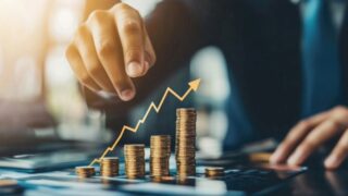 يد تشير إلى رسم بياني يظهر زيادة في الأرباح مع أكوام من العملات المعدنية تتصاعد في الارتفاع، مما يعكس مفهوم النمو المالي والنجاح في الأعمال.