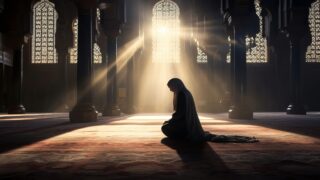 امرأة ترتدي الحجاب تجلس في الصلاة داخل مسجد، محاطة بأعمدة ومشاهد جميلة للزجاج الملون. أشعة الشمس تتسلل من النوافذ، مما يخلق جوًا هادئًا وروحيًا.