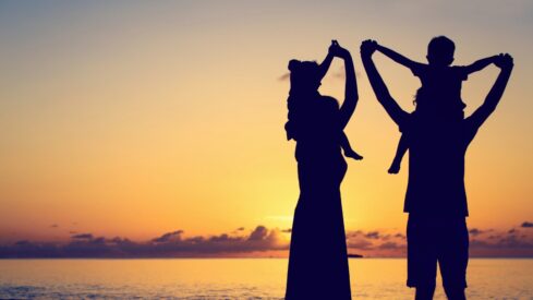 عائلة تحتفل بغروب الشمس، حيث تظهر silhouettes الأم والأب والطفل. السماء تتلون بألوان دافئة، مما يخلق مشهداً جميلاً يعكس اللحظات السعيدة والترابط الأسري.