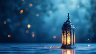 فانوس معدني مزخرف ينبعث منه ضوء دافئ، محاط بخلفية زرقاء ضبابية وبقع مضيئة. يضيف الأجواء السحرية والرومانسية للمشهد.