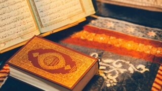 كتاب مفتوح للقرآن الكريم بجانب مصحف مغلق، موضوعة على سجادة مزخرفة.