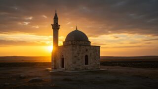 مسجد صغير ذو قبة ومئذنة، يقع في منظر خلاب عند غروب الشمس، السماء مغطاة بالسحب مع أشعة الشمس الذهبية تتسلل من خلفه، طبيعة هادئة تحيط بالمكان.