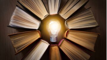 مصدر إلهام مع كتاب مفتوح ومصباح مضيء في المركز، محاط بكتب مغلقة مرتبة بشكل دائري. يعكس الصورة فكرة المعرفة والإبداع.