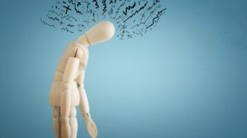 تمثال خشبي مائل للأمام، يعبر عن الإحباط أو القلق، مع رسومات متداخلة فوق رأسه تعكس مشاعر التوتر والضغط النفسي. الخلفية زرقاء بسيطة، مما يسلط الضوء على تعبير التمثال.