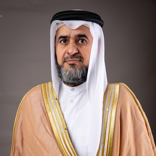 رجل يرتدي الزي التقليدي العربي، بما في ذلك الغترة والعقال، مع لحية رمادية، وخلفية رمادية بسيطة.