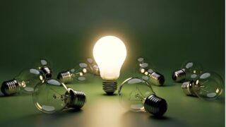 مصباح مضيء محاط بمصابيح غير مضاءة، خلفية خضراء، يرمز إلى الإبداع والابتكار.