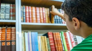 شاب يضع كتابًا في مكتبة مليئة بالكتب الملونة، مع التركيز على تفاصيل الكتب وأرفف المكتبة.