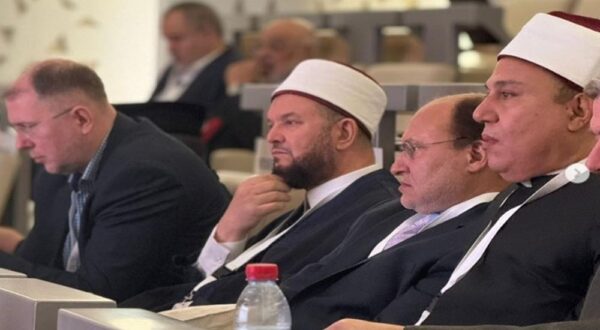 رجال يرتدون العمائم يجلسون في صفوف خلال مؤتمر، مع التركيز على التفاعل والاهتمام. تتواجد مجموعة من الحضور في الخلفية.
