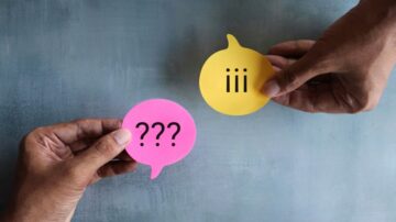 شخصان يحملان بطاقات ملونة، واحدة وردية تحتوي على علامات استفهام والثانية صفراء تحمل ثلاثة خطوط، في خلفية رمادية.