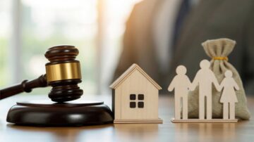 A wooden gavel rests on a table next to a miniature house, a bag of money, and a figure representing a family. The background suggests a legal setting, emphasizing themes of property, finance, and family law.