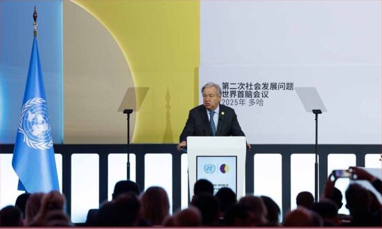 رجل يتحدث من منصة في مؤتمر دولي، مع وجود علم الأمم المتحدة خلفه. يظهر في الخلفية شعار المؤتمر وتفاصيل تصميم ملون.