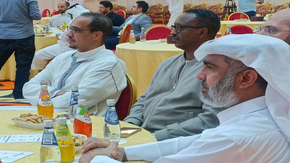 رجال يجلسون في قاعة احتفالية، يرتدون ملابس تقليدية. أمامهم طاولات مزينة بأطباق البسكويت والمشروبات الغازية. الأجواء تعكس تجمعًا اجتماعيًا أو حدثًا رسميًا في منطقة الشرق الأوسط.