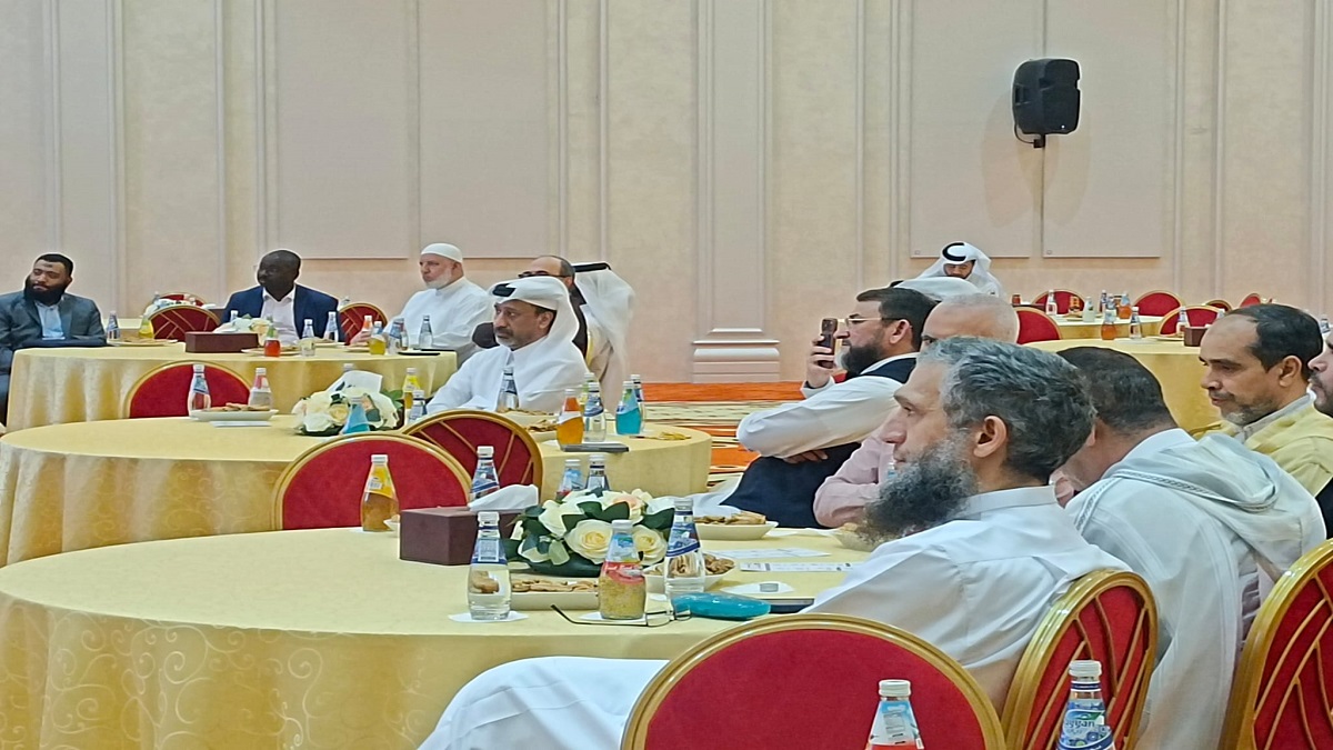 اجتماع يضم مجموعة من الرجال في قاعة مؤتمرات، يجلسون حول طاولات مستديرة مغطاة بأقمشة ذهبية. المشاركون يرتدون أزياء تقليدية، مع وجود زهور وزجاجات مياه على الطاولات.