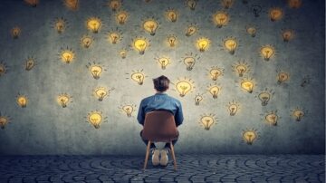 رجل يجلس على كرسي يواجه جدارًا مغطى برسوم لمصابيح مضيئة، مما يرمز إلى الإلهام والأفكار الجديدة.