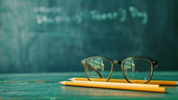 نظارات على مكتب مع أقلام رصاص صفراء، وخلفية تحتوي على سبورة خضراء. الصورة تعكس أجواء دراسية وترمز إلى التعليم.