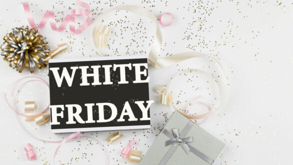 خلفية بيضاء مع نص كبير "الجمعة البيضاء" باللون الأسود، محاطًا بزينة ذهبية وشرائط ملونة، مع هدايا مزينة بأشرطة، مما يعكس أجواء الاحتفالات والتسوق.