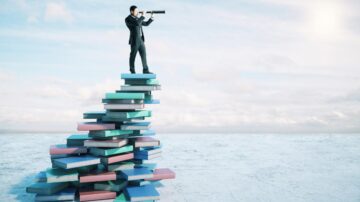 رجل يرتدي بدلة يقف على كومة من الكتب وينظر عبر منظار في سماء زرقاء. تعكس الصورة الطموح والسعي للمعرفة.