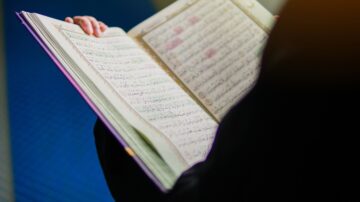 كتاب مفتوح يظهر صفحات مليئة بالكتابة العربية، مع تركز الضوء على النص. يبرز تصميم الكتاب بألوانه الزاهية وتفاصيله الفنية، مما يعكس أهمية النص الديني.