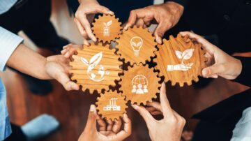 أيدي متعددة تحمل تروساً خشبية تحتوي على رموز تمثل الاستدامة والابتكار، مثل كوكب الأرض، ونباتات، ومصابيح، ويدين ترمزان إلى التعاون، مما يعكس جهود العمل الجماعي نحو مستقبل بيئي أفضل.