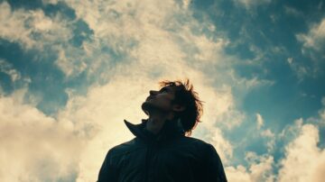 شاب ينظر إلى السماء مع سحب بيضاء وزرقاء، يعكس شعورًا بالتأمل والتفكير.