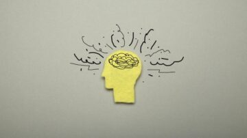 رسم توضيحي لرأس بشري مصنوع من ورقة ملونة باللون الأصفر مع رسومات تعبيرية توحي بالتفكير والإبداع، مع وجود رسم لدماغ في الجزء العلوي. الخلفية رمادية بسيطة تبرز التصميم.