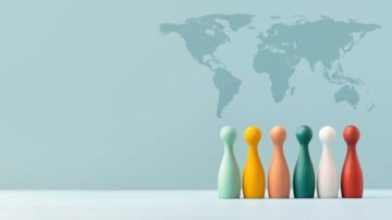 تظهر الصورة مجموعة من قطع اللعب الخشبية الملونة، مرتبة في صف، مع خريطة العالم باهتة في الخلفية. الألوان تشمل الأخضر، الأصفر، البرتقالي، الأبيض، والأحمر، مما يرمز إلى التنوع والتواصل العالمي.