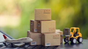 صناديق شحن صغيرة مكتوب عليها "هش" و"احفظ جاف" بجانب طائرة نموذجية ومركبة شحن صغيرة، مع خلفية طبيعية غير واضحة.