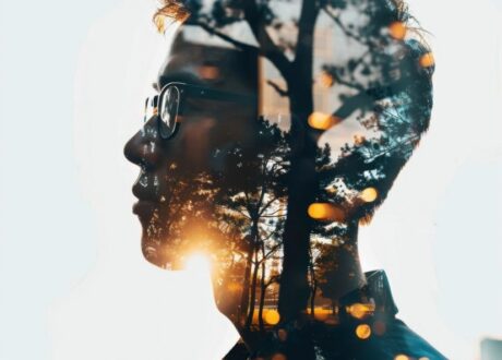 صورة مزدوجة لشخص يرتدي نظارات، مع غابة وأشجار في الخلفية. تظهر أشعة الشمس في الأفق، مما يخلق تأثيرًا فنيًا يجمع بين الطبيعة والإنسان.