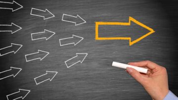 إشارة إلى الاتجاه مع سهم برتقالي على خلفية سبورة، محاطة بأسهم بيضاء تشير إلى الاتجاه المعاكس. يد تحمل طبشورة توضح الفكرة.
