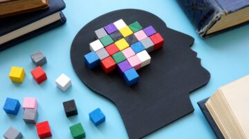 شكل رأس بشري مصنوع من الخشب مع مكعبات ملونة تمثل التفكير والإبداع، محاط بكتب ومكعبات صغيرة ملونة. صورة تعبر عن علم النفس والتعلم.
