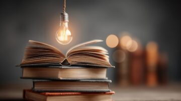 كتاب مفتوح موضوع على كومة من الكتب، مع مصباح مضيء معلق فوقه، خلفية ضبابية مع نقاط ضوء لامعة.