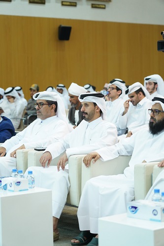 مشاركون في مؤتمر يرتدون الزي التقليدي الإماراتي، يجلسون في قاعة معاصر. يظهر في الصورة عدد من الرجال بملابس بيضاء وسوداء، بعضهم يرتدي النظارات. الخلفية تحتوي على جدران خشبية وديكور بسيط.