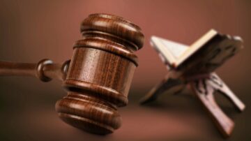 مطرقة قانونية خشبية بجانب مصحف على حامل، مع خلفية محايدة. تعبير عن العدالة والدين.