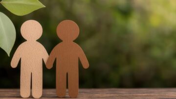 شخصيتان خشبيتان تمثلان التنوع والاندماج، واقفتان جنبًا إلى جنب على سطح خشبي، مع خلفية خضراء ضبابية.