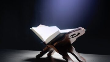 كتاب مفتوح على حامل خشبي مع إضاءة موجهة، خلفية داكنة.