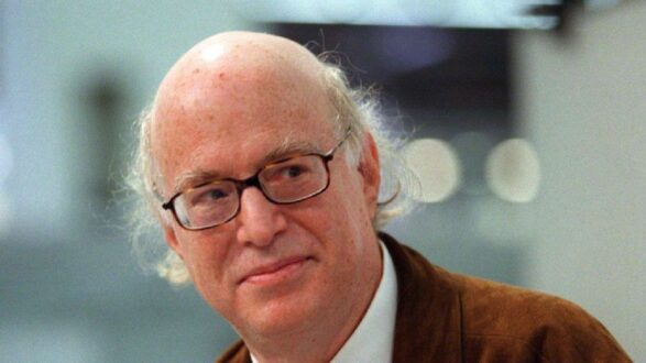 رجل مسن ذو شعر رمادي خفيف ونظارات، مبتسم في بيئة غير محددة. يعكس الصورة طابعاً ودوداً ومتفائلاً، مما يعزز من جاذبيتها.