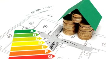 خطة منزلية مع نموذج منزل صغير بغطاء أخضر، موضوعة فوق أكوام من العملات المعدنية. يظهر مقياس كفاءة الطاقة بألوان تتراوح من الأخضر إلى الأحمر، مما يشير إلى تصنيفات من A إلى G. تعكس الصورة العلاقة بين الاقتصاد المنزلي وكفاءة الطاقة.