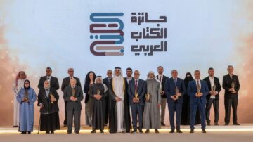 مراسم توزيع جوائز الكتاب العربي، تجمع لعدد من الفائزين والمكرمين على منصة احتفالية. يظهر في الصورة مجموعة متنوعة من الأشخاص، بما في ذلك رجال ونساء من مختلف الأعمار، يحملون الجوائز. الخلفية تحمل شعار الجوائز باللغة العربية، مما يعكس أهمية الحدث الثقافي والأدبي.