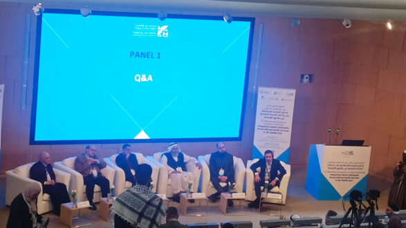 صورة لندوة تحتوي على ستة متحدثين يجلسون على كراسي بيضاء في مقدمة منصة. خلفهم شاشة كبيرة تعرض عنوان "الجلسة 1: أسئلة وأجوبة". الحضور في الأمام يستمعون للنقاش.