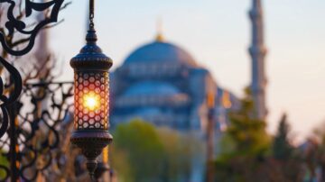 Colorful lantern hanging in the foreground with a blurred view of the Hagia Sophia in the background, showcasing its iconic dome and minarets during sunset.