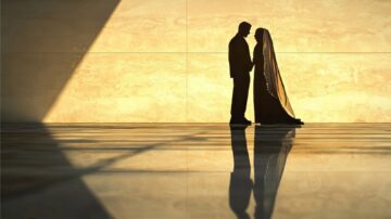 Silhouette of a couple holding hands against a softly lit wall, showcasing their romantic connection. The scene features elegant wedding attire and reflections on the polished floor, creating a serene and intimate atmosphere.