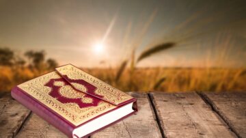 A beautifully bound book with a gold embossed cover rests on a wooden table, set against a blurred background of a golden sunset over a field. The scene conveys a peaceful and serene atmosphere, perfect for reading or reflection.