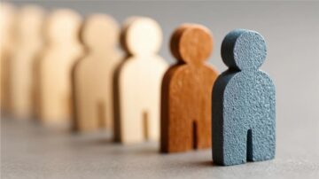 أشكال خشبية تمثل مجموعة من الأشخاص، مع تباين في الألوان. يظهر شخص بلون أزرق في المقدمة، بينما تظهر أشكال بألوان طبيعية أخرى في الخلفية. التصميم يعكس التنوع والتميز في المجموعة.