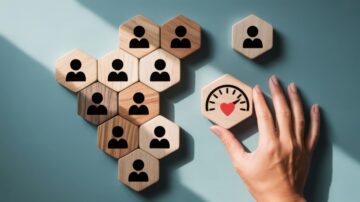 صورة توضح مجموعة من قطع الخشب السداسية الشكل، تحتوي على رموز لأشخاص، مع وجود يد تضع قطعة خشبية تحمل رمز عداد قلب. تعبر الصورة عن قياس المشاعر أو الارتباط الاجتماعي.