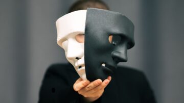 امرأة تحمل قناعًا أبيض وأسود، يعبر عن التناقض بين الأدوار أو المشاعر. خلفية رمادية تضيف عمقًا للصورة، مما يعكس موضوع الهوية والتغيير.