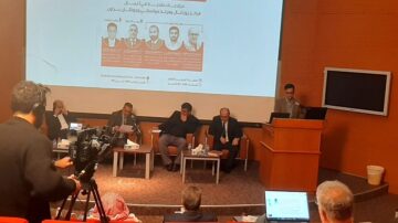 مؤتمر حول الاستثمارات في التعليم العالي، مع متحدثين يتناولون مواضيع تتعلق بالتعليم والتكنولوجيا في الوطن العربي. يظهر في الصورة مجموعة من المحاضرين في منصة، وجمهور يجلس في الصفوف الأمامية. تم تصوير الحدث من زاوية جانبية مع معدات تسجيل الفيديو.