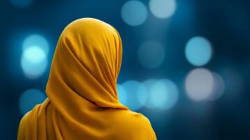 Woman wearing a yellow hijab, facing away from the camera, with a blurred blue background featuring soft, colorful bokeh lights. This image captures a serene and contemplative atmosphere, emphasizing the elegance of cultural attire.
