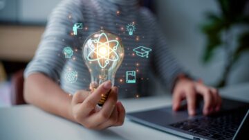 يدٌ تحمل مصباحًا مضيئًا يظهر رموزًا تمثل العلم والتكنولوجيا، مثل الذرة، والفكر، والتعليم، مع جهاز كمبيوتر محمول في الخلفية. تعبير عن الإبداع والابتكار في مجال التعليم والتكنولوجيا.
