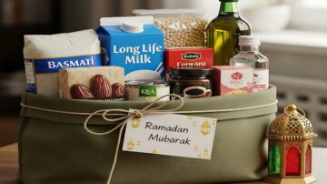 سلة تحتوي على مواد غذائية متنوعة للاحتفال برمضان، تشمل الأرز البسمتي، والحليب طويل الأجل، وزيت الزيتون، ومكسرات، وحلويات. السلة مزينة ببطاقة مكتوب عليها "رمضان مبارك" وفانوس رمضاني ملون.