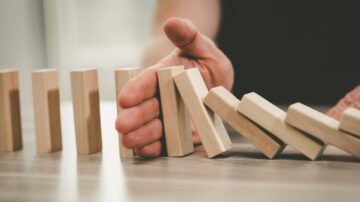 يد تظهر يداً تُوقف قطع دومينو خشبية تتساقط، مع التركيز على الحركة والتحكم. تعكس الصورة مفهوم التوازن والسيطرة في مواجهة الفوضى.